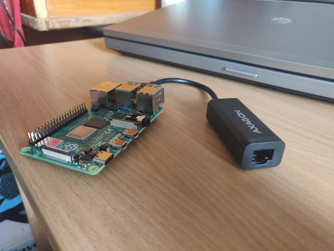 Raspberry Pi 4 board connected to a USB-to-Ethernet adapter, placed on a desk next to a laptop.