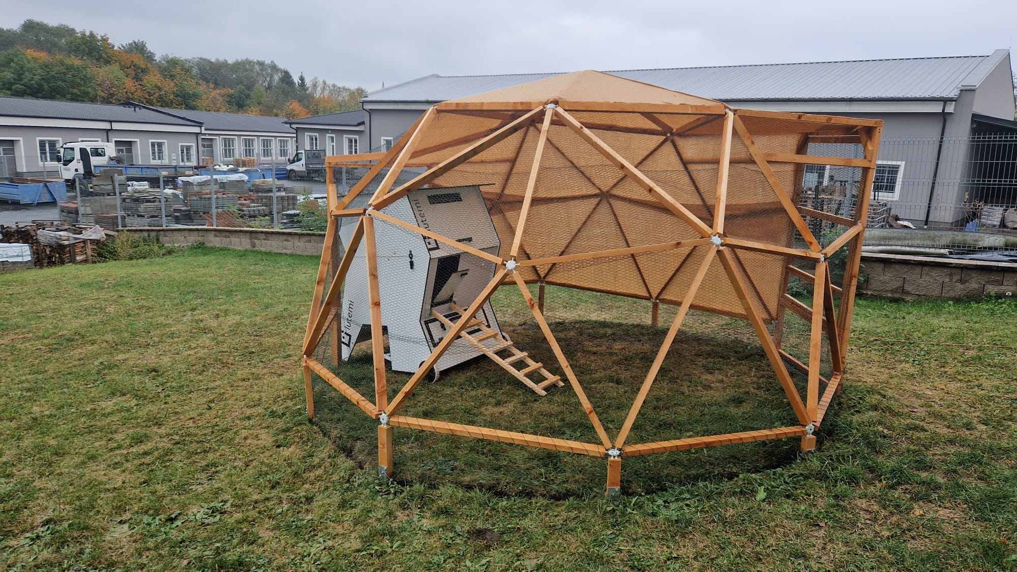 Early prototype of a wooden smart henhouse structure installed outdoors near industrial buildings, illustrating physical hardware deployment requiring on-site debugging.